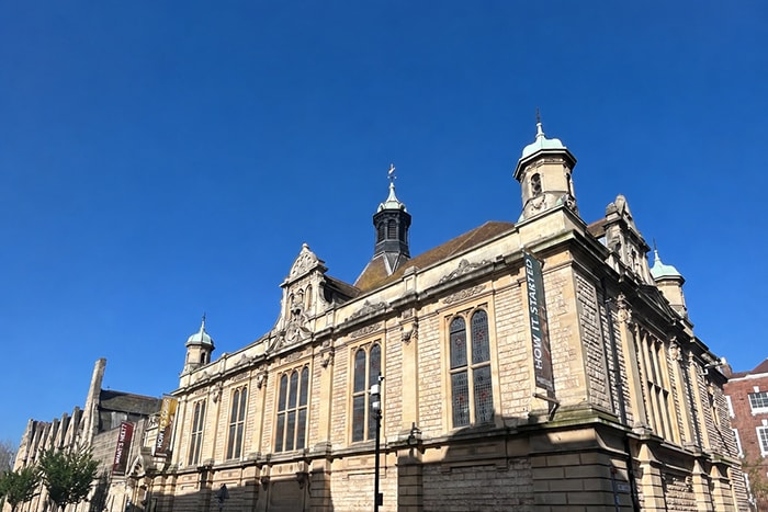 Ornate Victorian stone building in Gloucester with copper-domed turrets, decorative gables, and tall arched windows, photographed against a clear blue sky.
